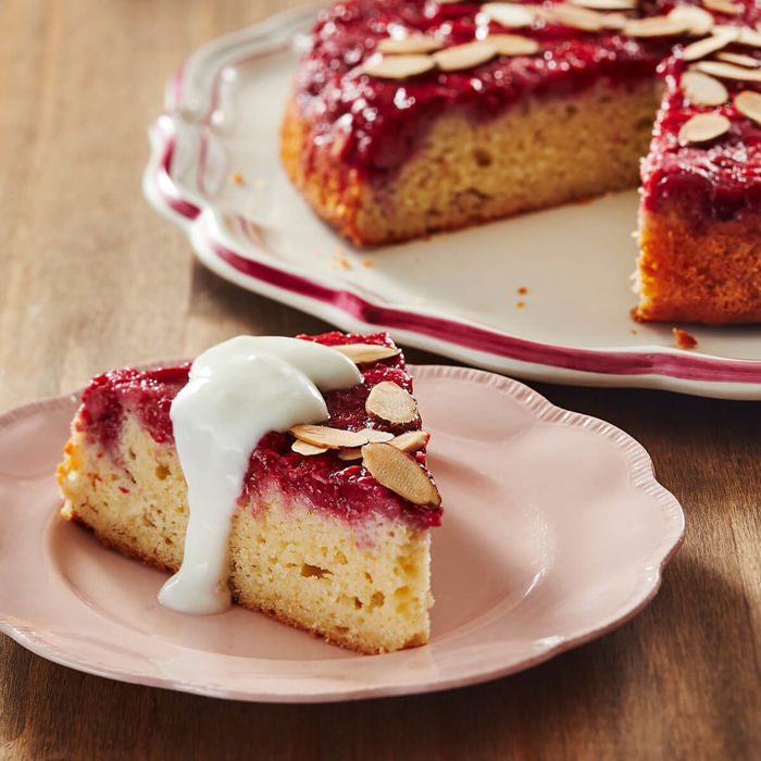 Part de gâteau renversé au yogourt et aux framboises garni d’amandes grillées rôties, servie avec une cuillérée de yogourt vanillé sur le dessus.  