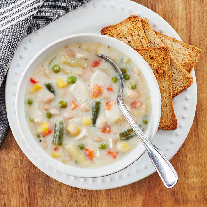 Bol de soupe crémeuse au poulet, haricots blancs et légumes colorés, servie avec des craquelins de blé entier.