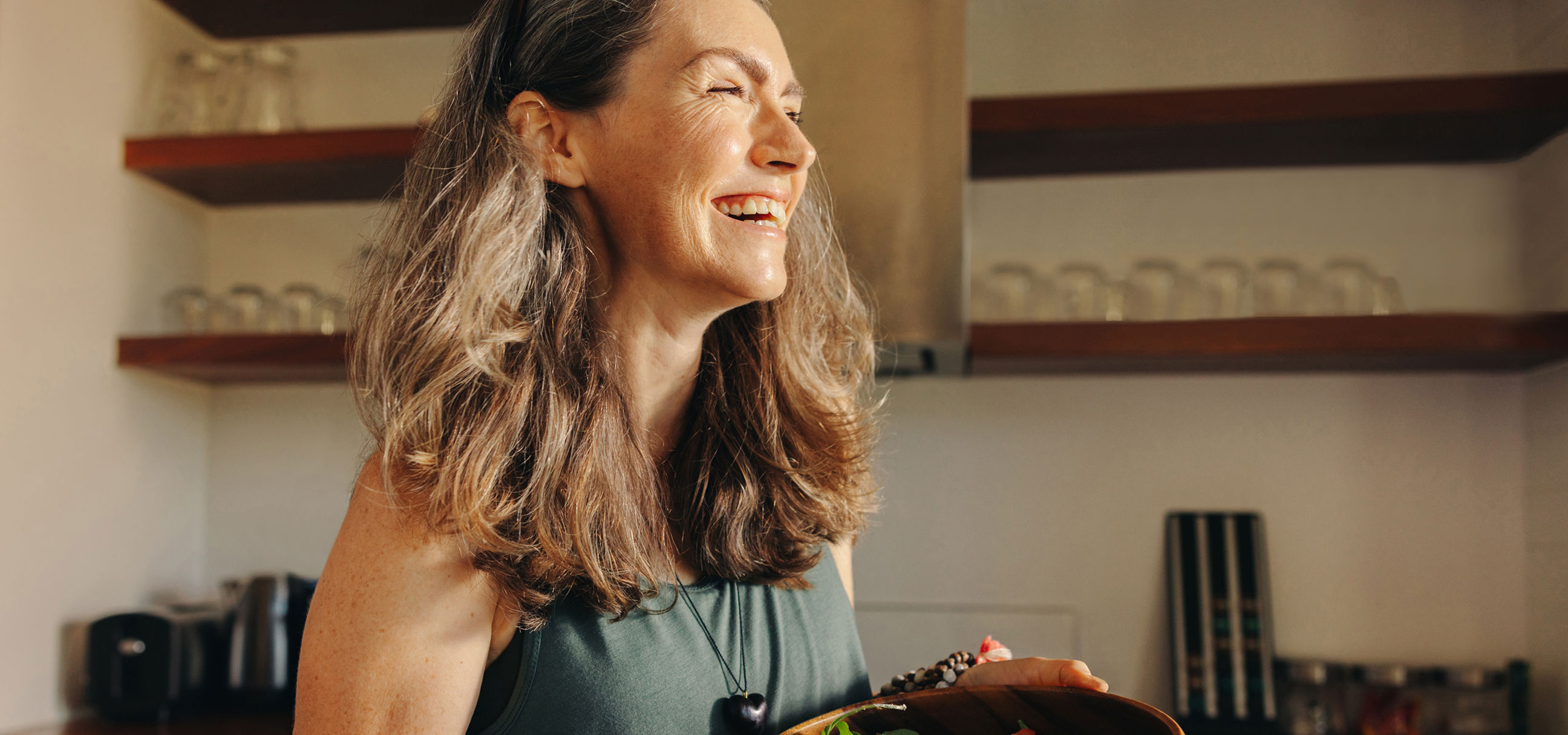 Une femme souriante servant un bol de salade dans sa cuisine.
