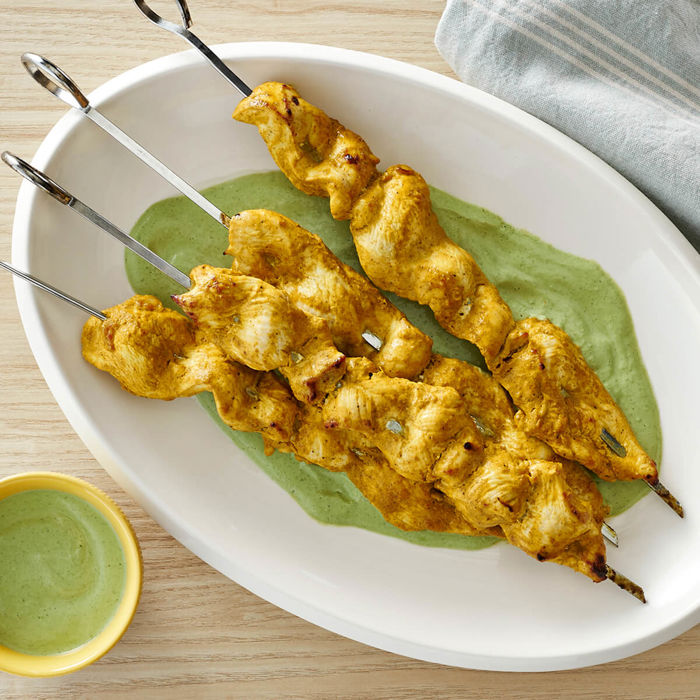 Assiette avec des brochettes de poulet au citron sur une sauce verte au yogourt et aux fines herbes.