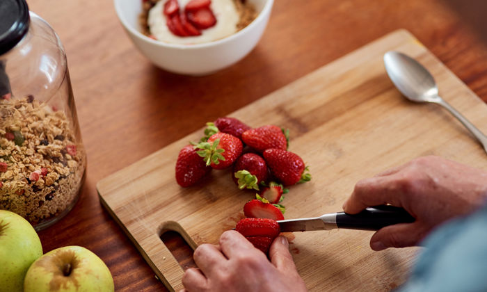 Alimentation équilibrée : sur le comptoir de la cuisine, des fraises sont coupées pour préparer un bol de yogourt garni de granola maison. 