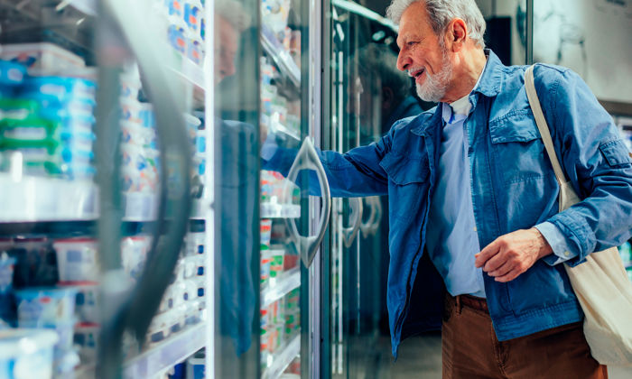 Coûts des aliments : un homme choisit un produit laitier dans le rayon réfrigéré d’une épicerie. 