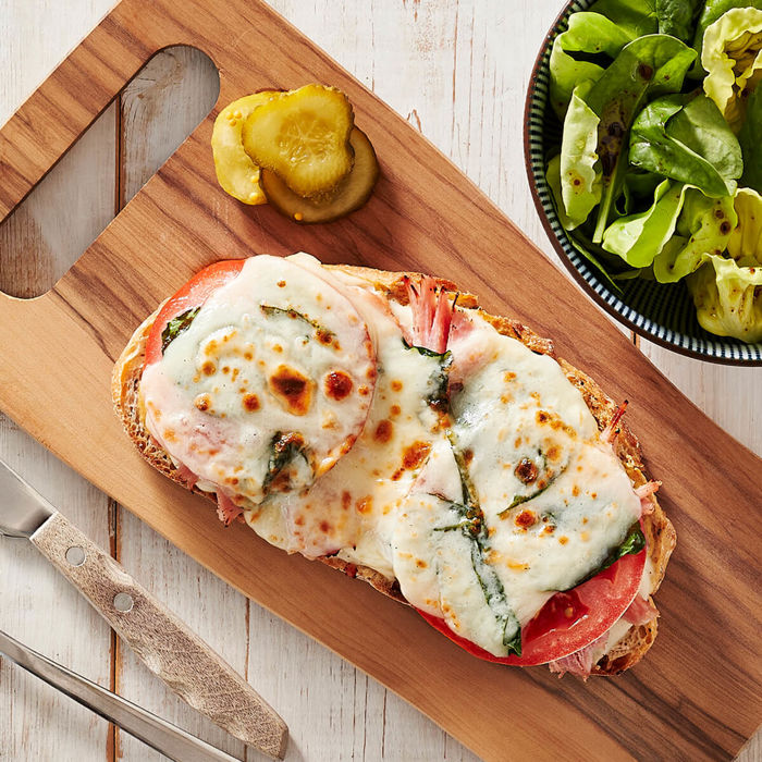 Croque-monsieur au jambon garni de fromage, servi sur une planche de bois et accompagné d’une salade verte.  