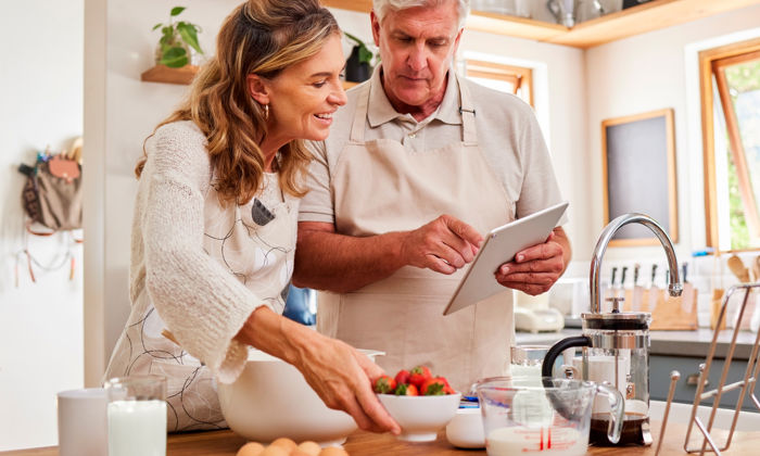 Protéines : une femme et un homme cuisinent en consultant une tablette. Il y a des fraises, des œufs et du lait sur le comptoir. 